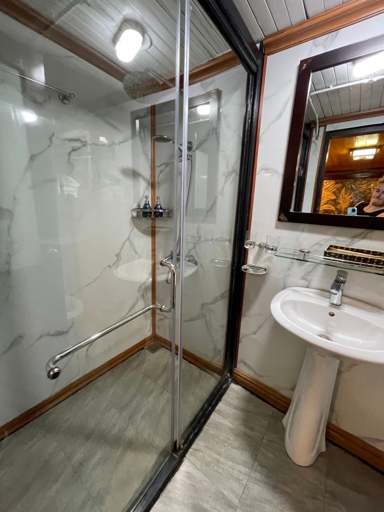 A modern bathroom featuring a glass shower enclosure with a handheld showerhead, a marble-patterned wall, and a white sink with a mirror above it.